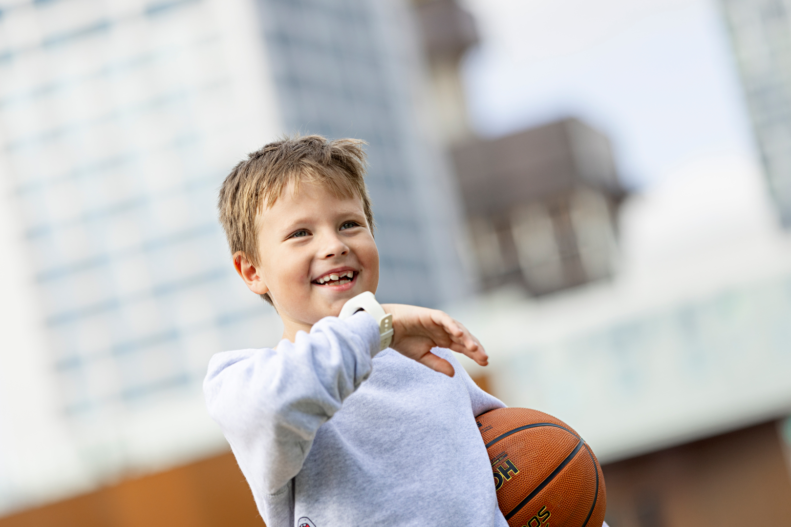 hymyilevä vaaleahiuksinen poika ulkona koripallo kainalossa puhumassa kellopuhelimeen