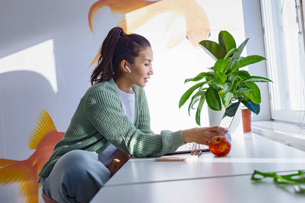 nainen istuu työpöydän ääressä ja katselee tietokonetta, vieressä pöydällä viherkasvi