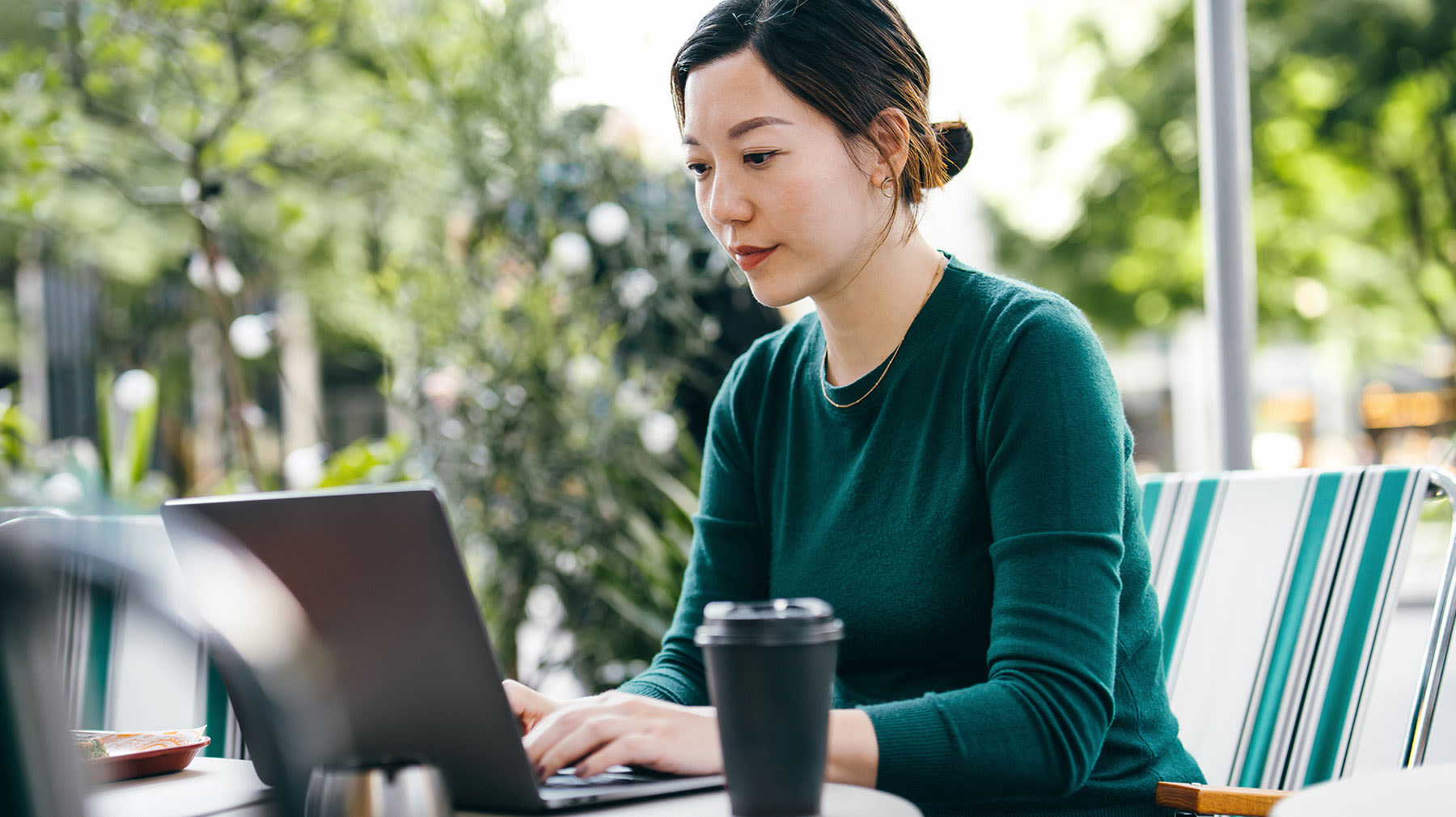 Nainen työskentelee tietokoneella ulkoilmakahvilassa