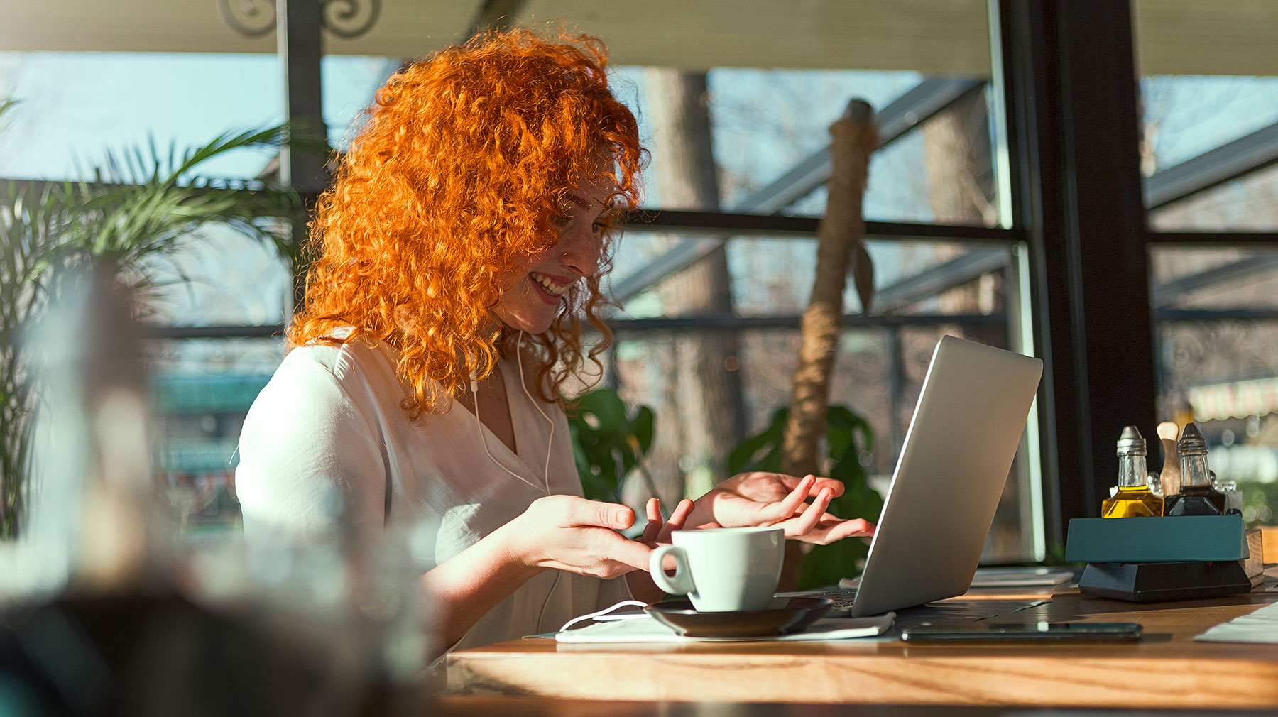 Nainen istuu kahvilassa ja puhuu etäkokouksessa