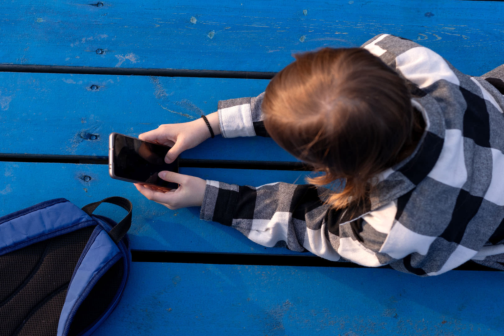 Ruutupaitainen poika makaa sängyllä ja selaa puhelinta
