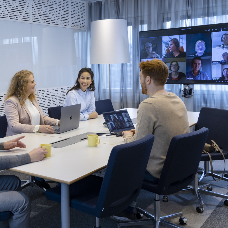 Neljä ihmistä neuvotteluhuoneessa, lisäksi mukana osallistujia myös Teamsin kautta