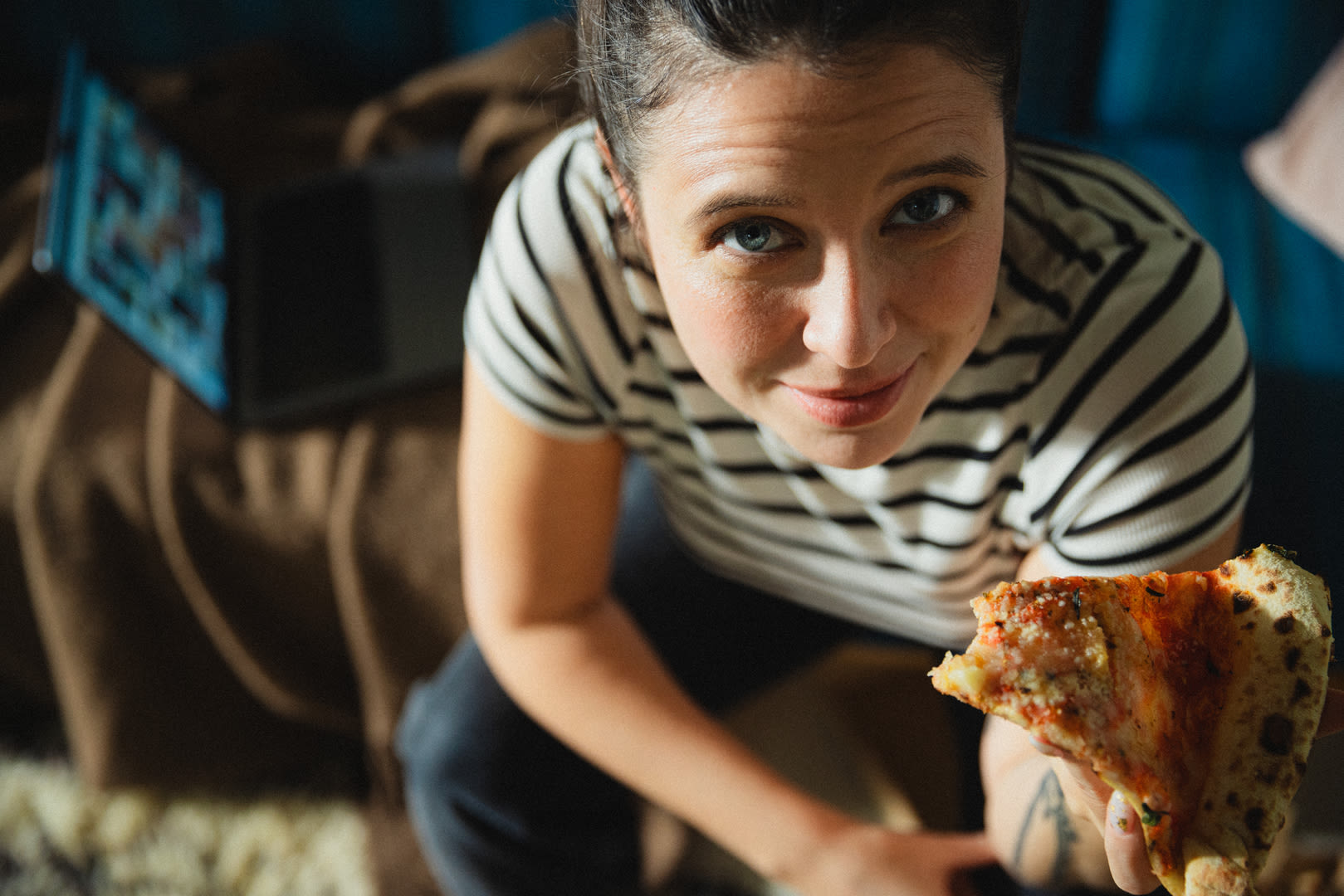 nainen katsoo kameraa pizza kädessään