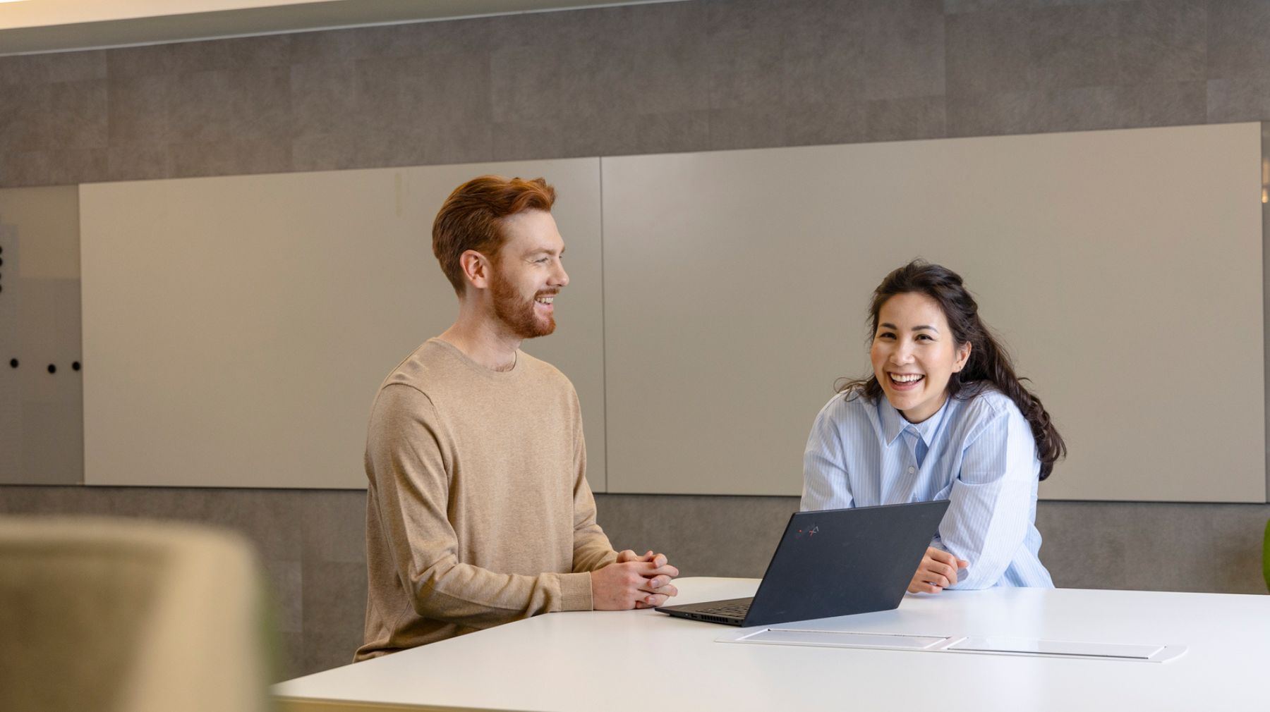 Mies ja nainen kannettavan tietokoneen äärellä nauramassa, keskustelun aiheena datalla johtaminen tekoälyn aikakaudella