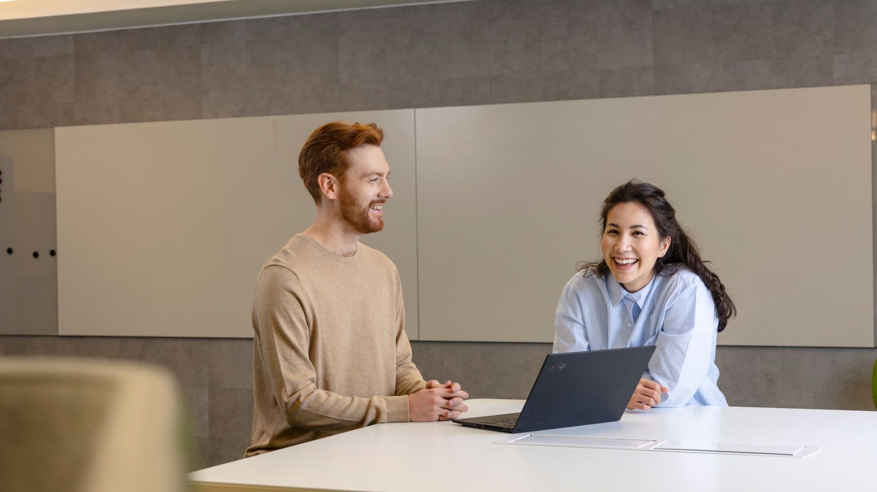 Mies ja nainen kannettavan tietokoneen äärellä nauramassa, keskustelun aiheena datalla johtaminen tekoälyn aikakaudella