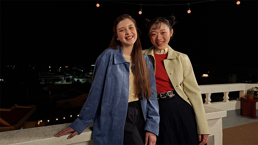 kaksi hymyilevää nuorta naista poseeraa ulkona pimeällä