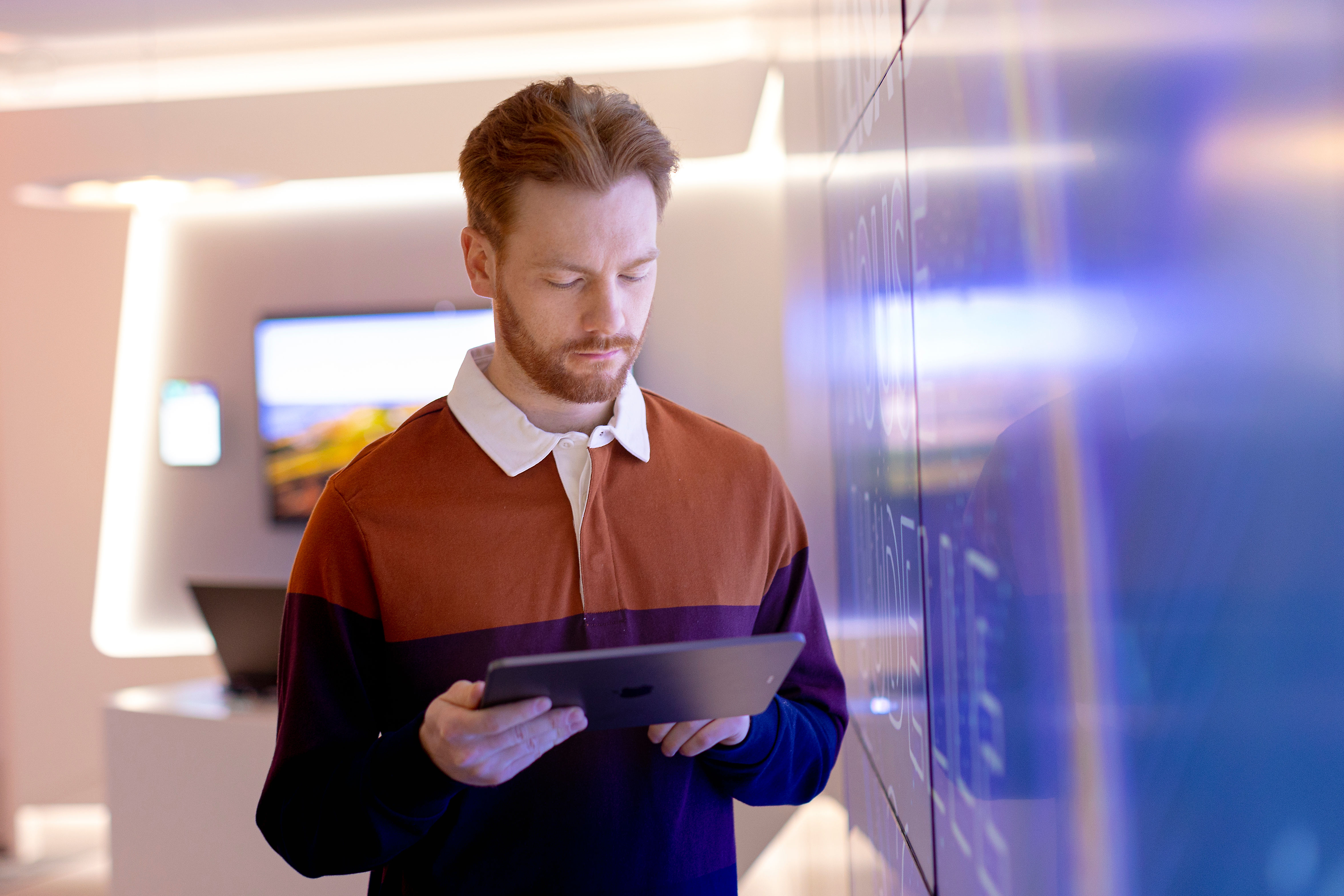 keski-ikäinen mies seisoo sinisen seinän vieressä ja katsoo käsissään olevaa tablettia
