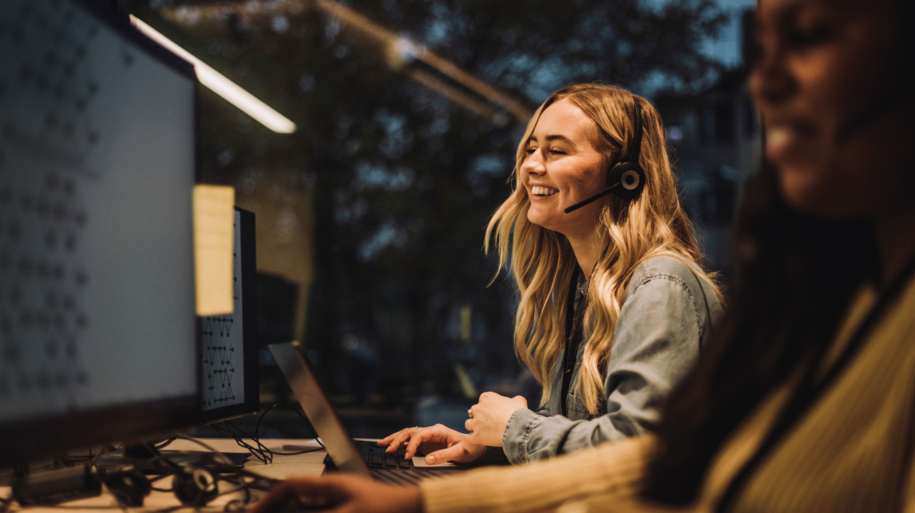 Service Desk -asiantuntija työskentelee tietokoneella kuulokemikrofoni päässä modernissa toimistossa ja keskustelee asiakkaan kanssa.