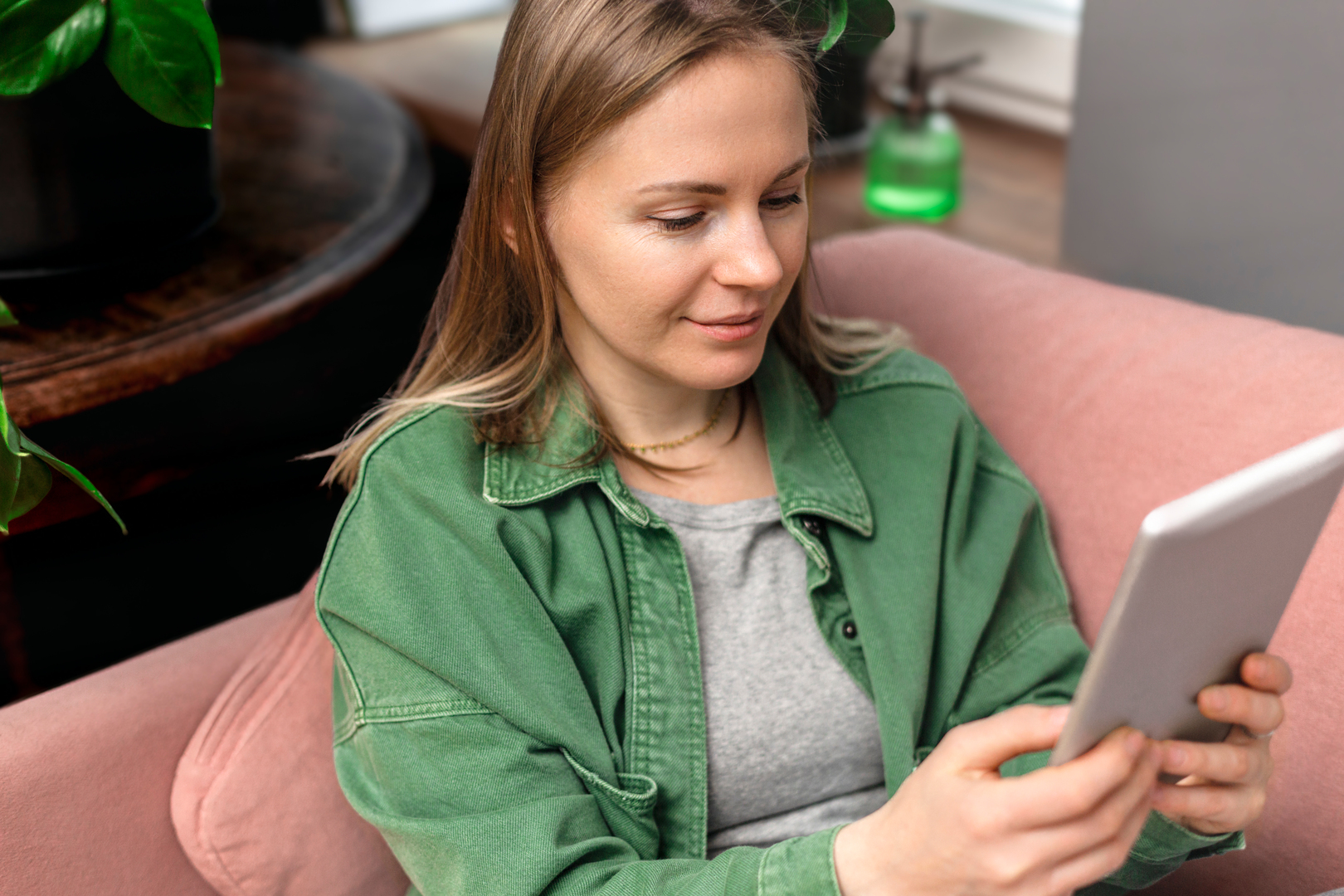 nainen istuu sohvalla ja selaa tablettia