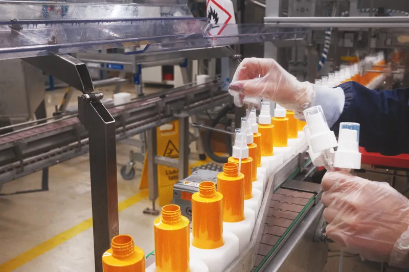 Kosmetiikkatuotteiden pulloja täytetään ja suljetaan Lumenen tuotantolinjalla teollisessa ympäristössä.