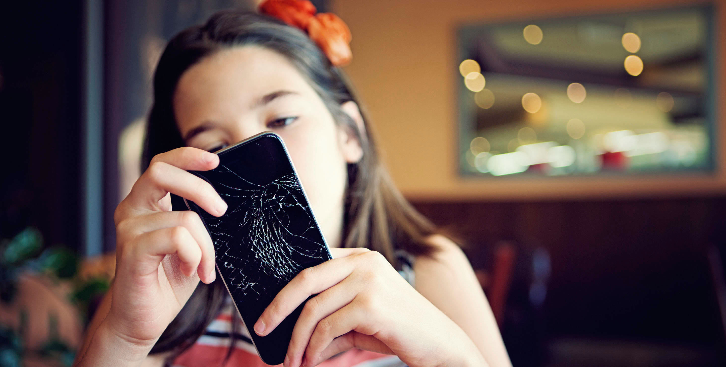 Aasialaistaustainen pikkutyttö pitelee puhelinta, jonka näyttö on rikkoutunut