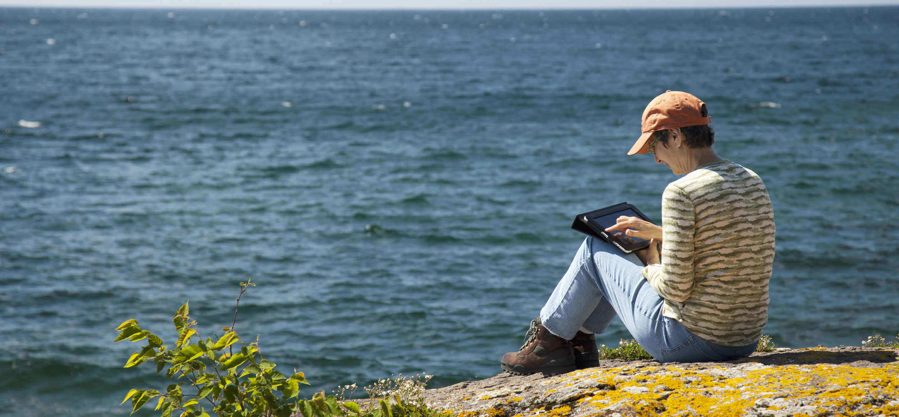 Henkilö istuu kalliolla tabletti kädessä.