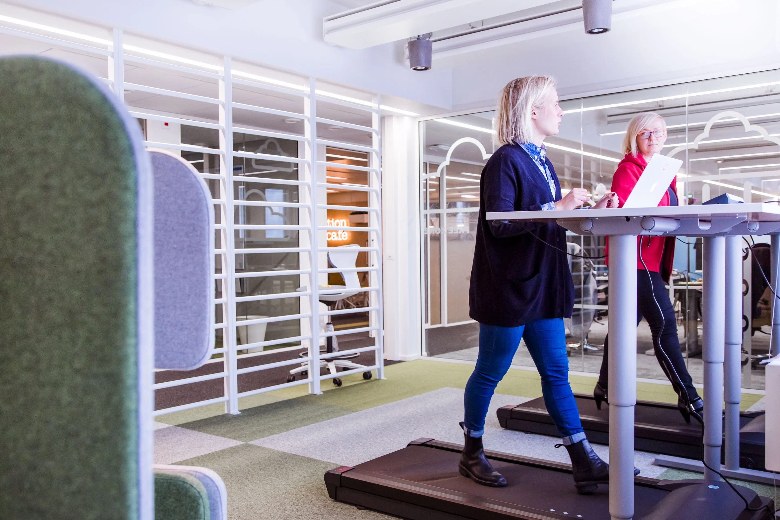 Naiset ovat palaverissa sähköpöydän ääressä kävellen samalla juoksumatolla - tulevaisuuden työtilojen tulisi vastata muuttuvia tarpeita.