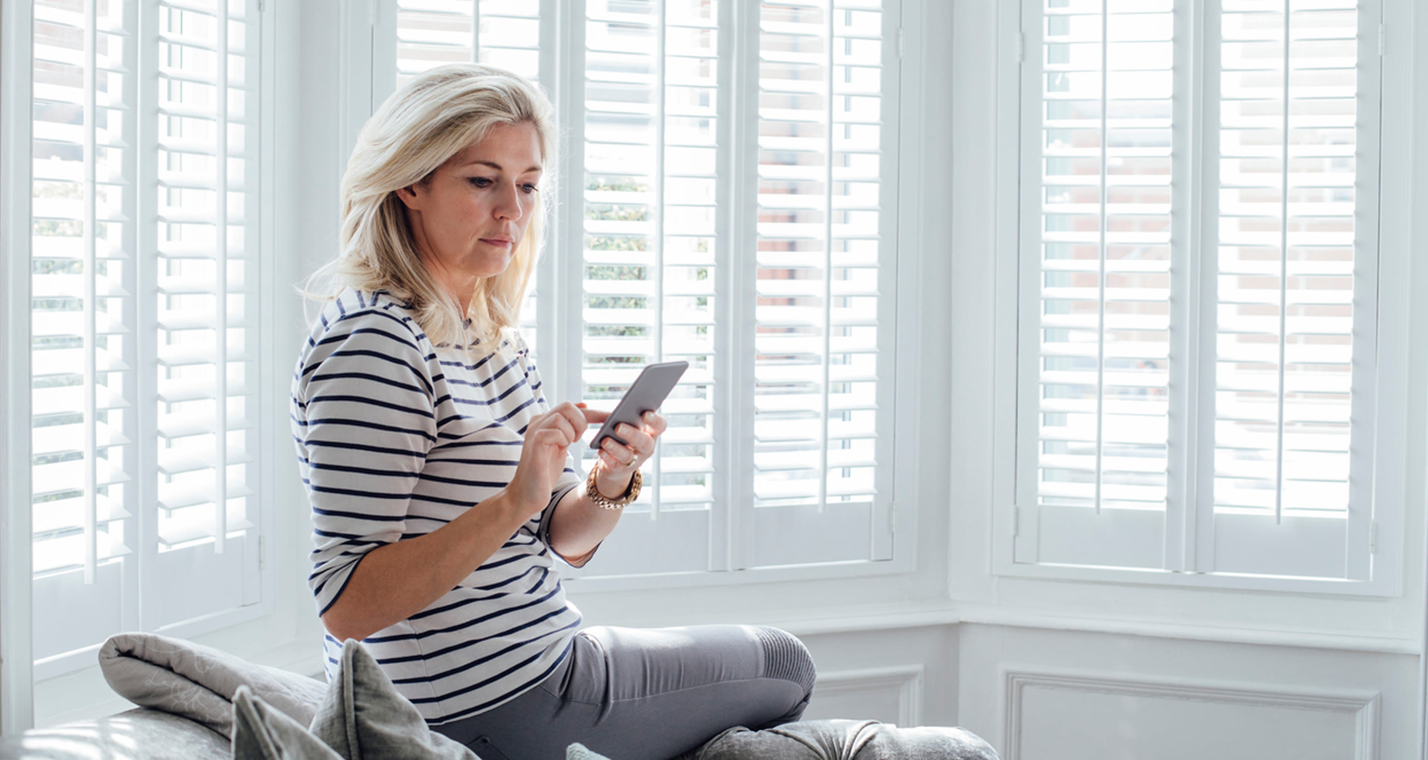 Nainen katselee sohvalla älypuhelintaan.