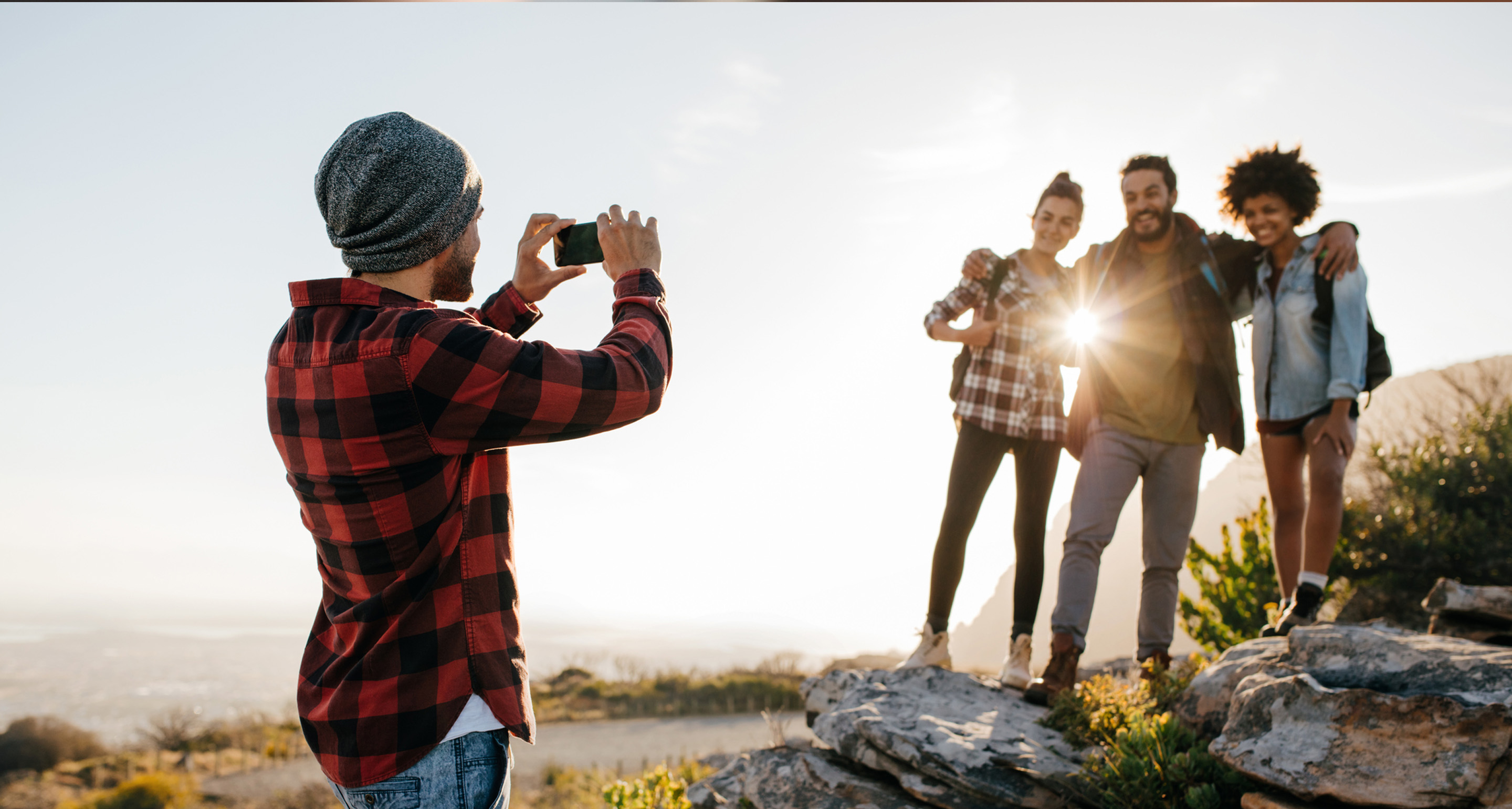 mies seisoo selin kameraan ja ottaa kuvaa kolmen miehen porukasta auringonlaskua vasten