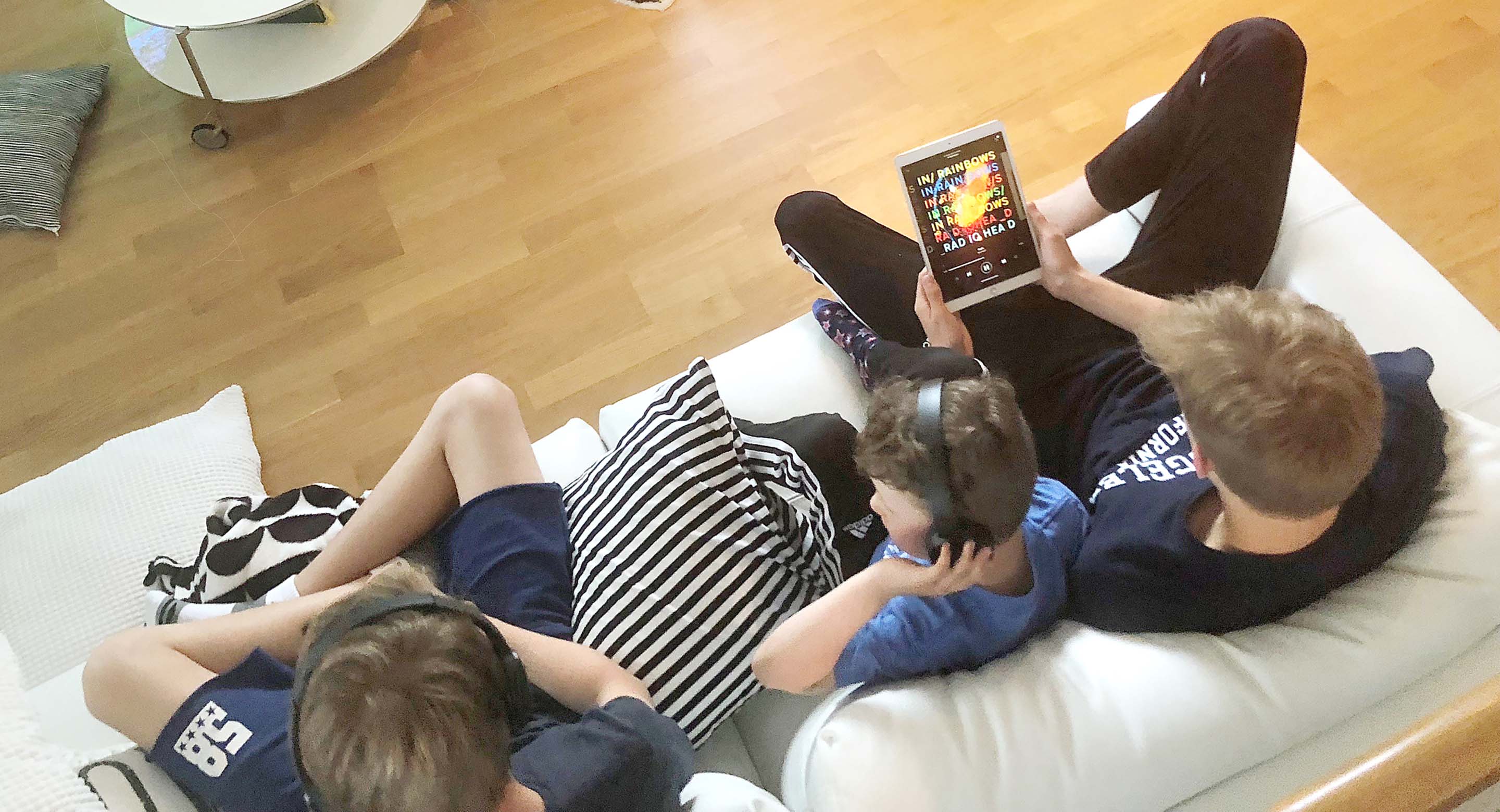 Perhe istuu sohvalla ja selaa puhelimia, kuva otettu yläviistosta takaapäin