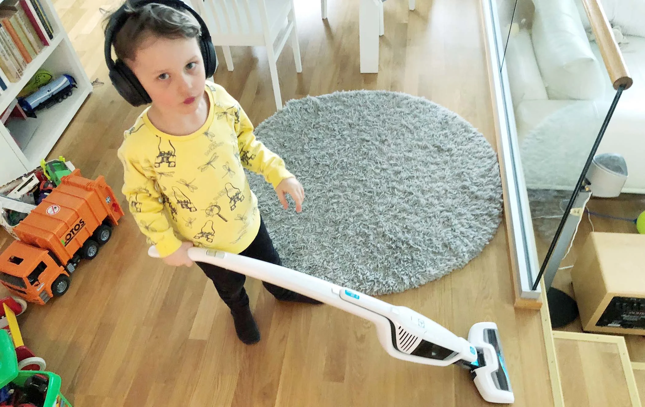 Lapsi mustat kuulokkeet päässä ja leikki-imuri kädessä kotona. 