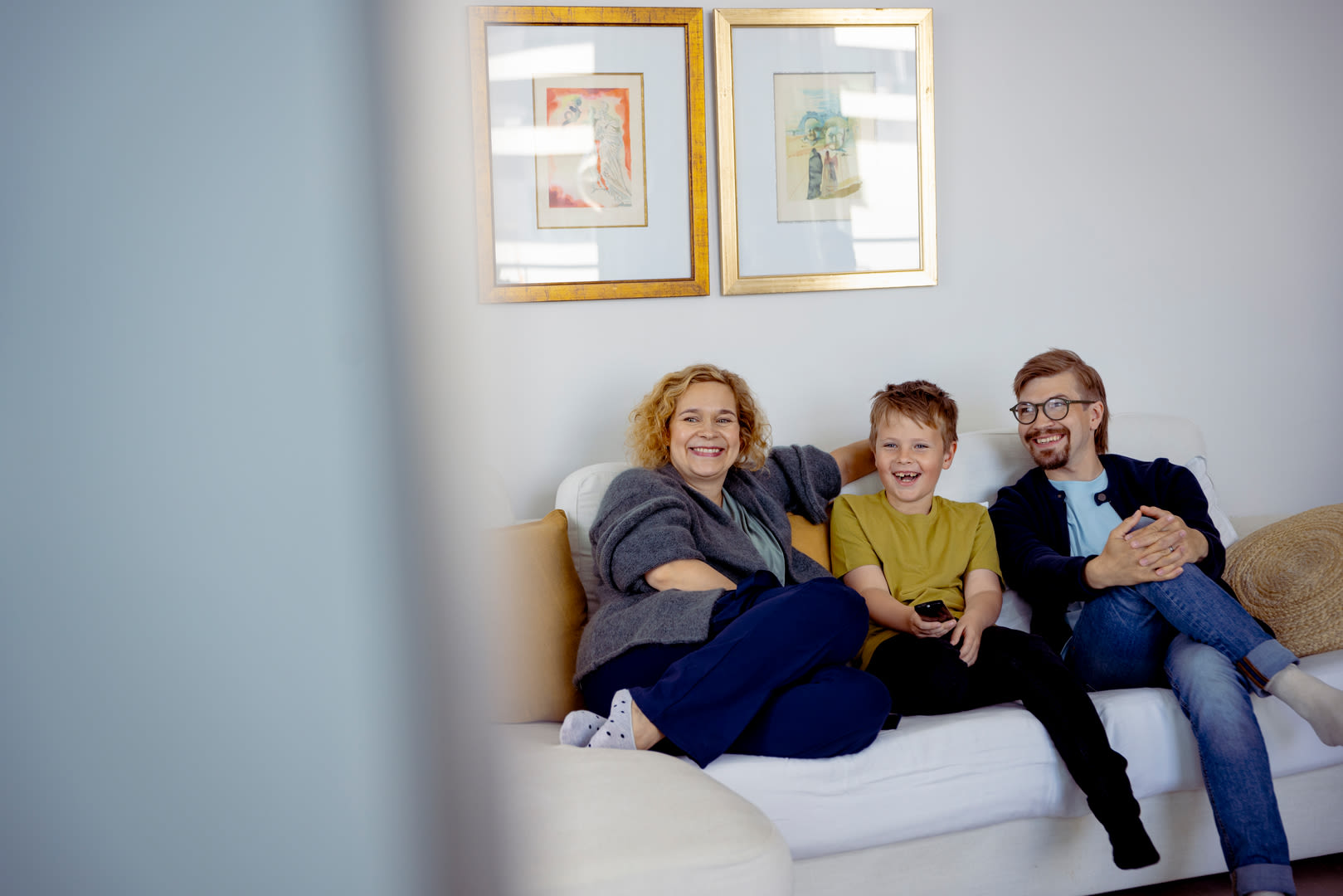 äiti, poika ja isä katsovat televisiota sohvalla