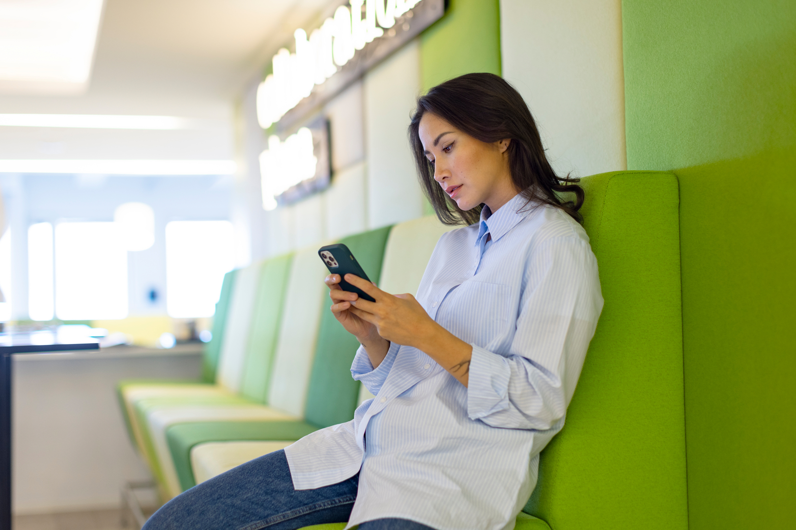 nainen nojaa toimistolla seinään ja katsoo puhelintaan