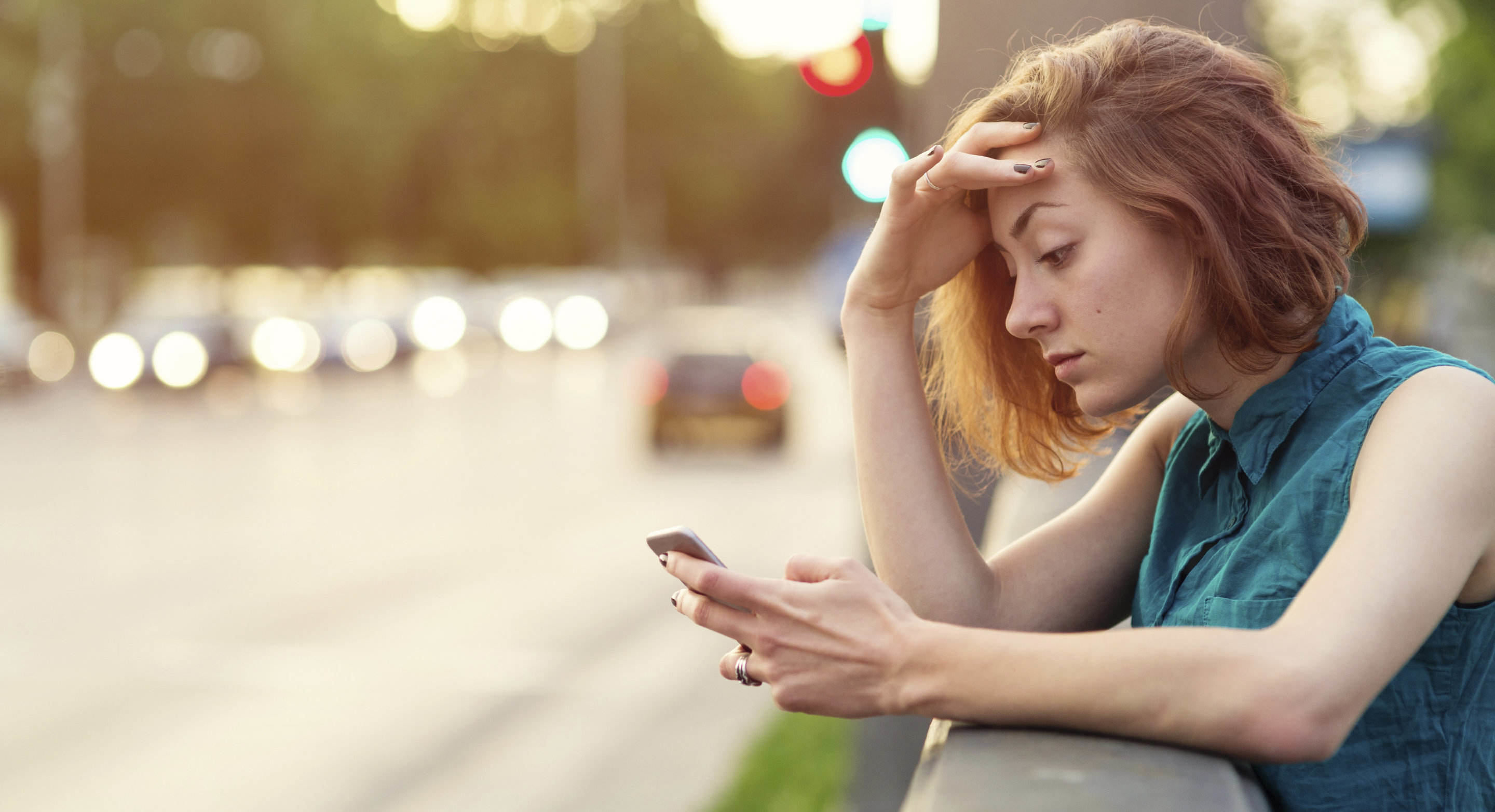 Nainen nojaa kaiteeseen autotien reunalla ja katsoo puhelintaan