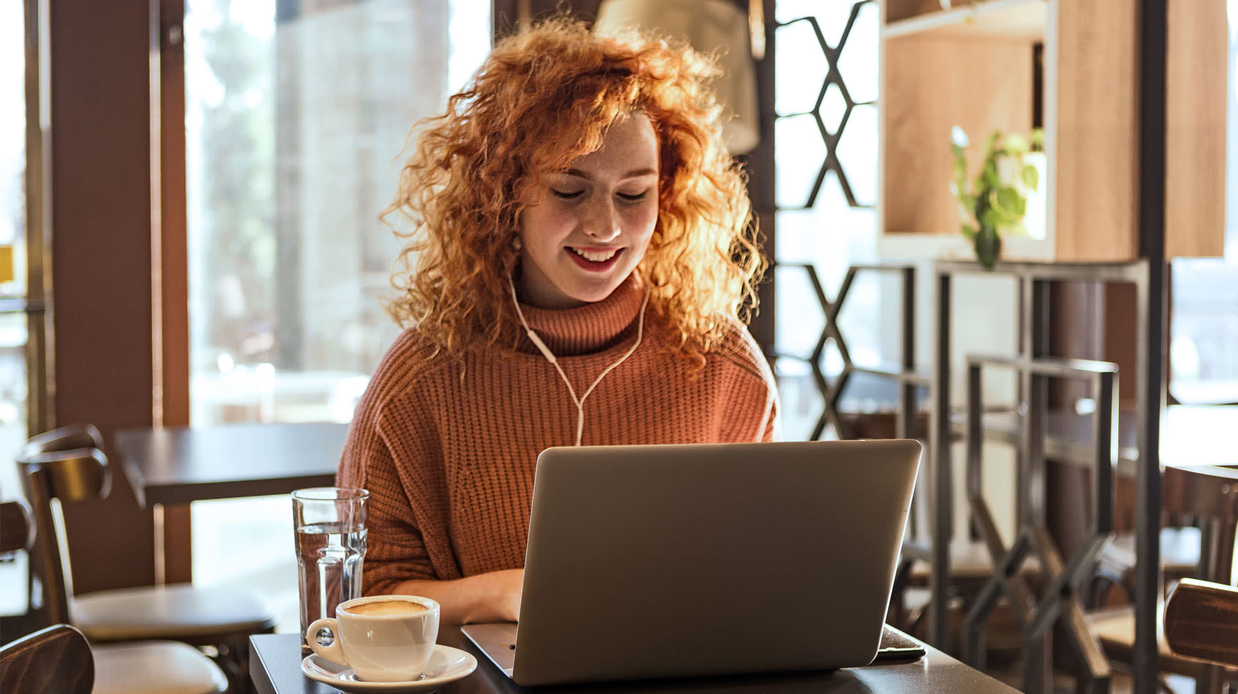 Hymyilevä nainen tekee töitä kahvilassa kannettavalla tietokoneella.