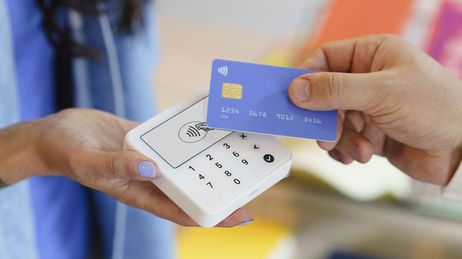 Nainen pitää kädessään langatonta maksupäätettä ja toinen henkilö maksaa ostostaan pankkikortilla.