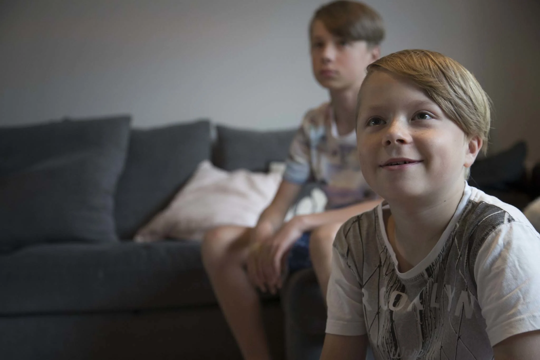 Kaksi poikaa katsoo televisioruutua. Vanhempi pojista istuu sohvalla, nuorempi hänen edessään lattialla.