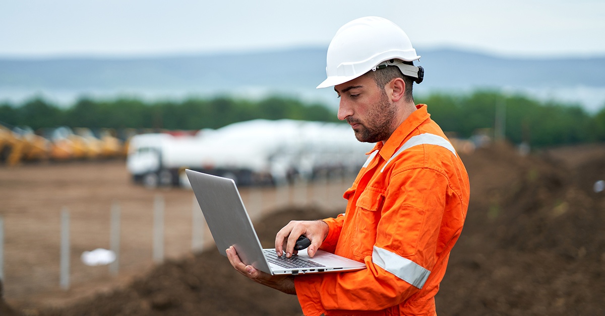 Mies työskentelee kannettavalla tietokoneella työmaalla. Paikkatiedon hyödyntäminen.