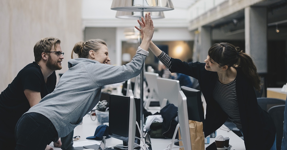 Iloiset toimistotyöntekijät lyövät kättä onnistumisen merkiksi. IT-ympäristö.