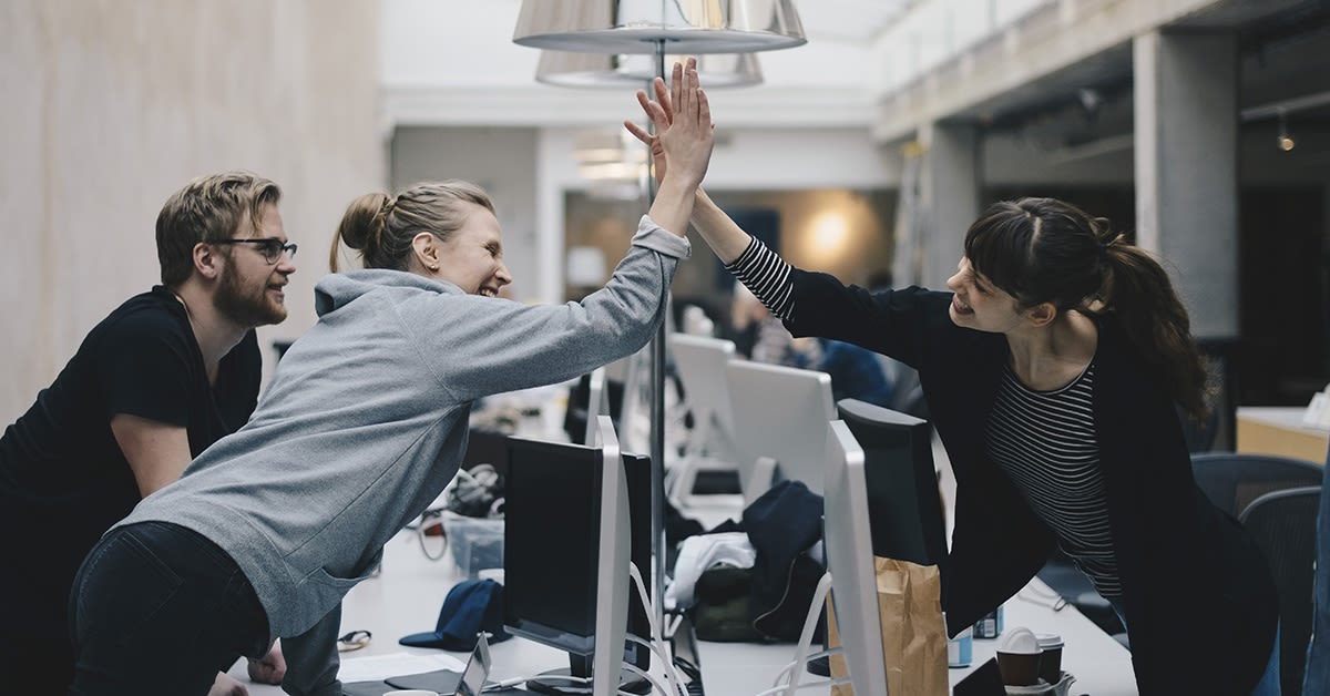 Iloiset toimistotyöntekijät lyövät kättä onnistumisen merkiksi. IT-ympäristö.