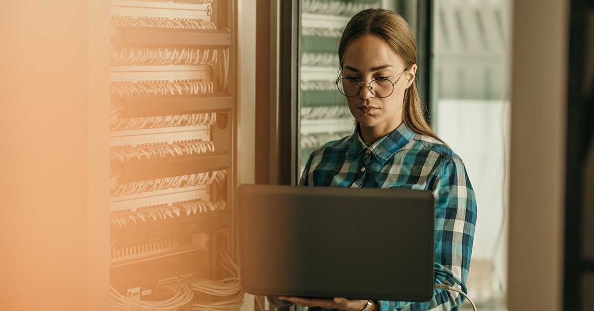 Nainen työskentelee kannettavalla tietokoneella datakeskuksessa. Hybridipilven keskitetty hallinta.
