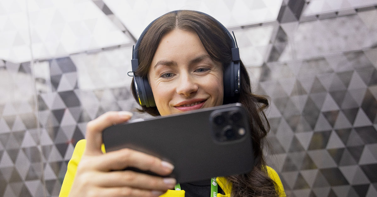 Nainen katsoo älypuhelinta kuulokkeet korvilla. Työpaikan digitalisointi.