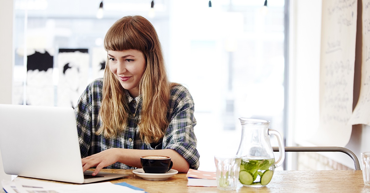 Näin VPN suojaa tietosi vieraassa verkossa. Nainen työskentelee valoisassa kahvilassa tietokoneella.