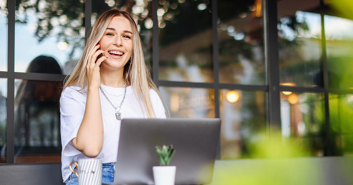 Nainen puhuu puhelimeen kahvilassa ja työskentelee koneella. Yrittäjän paikkariippumaton työ.