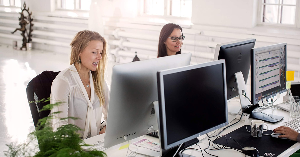 Naiset työskentelevät toimistossa tietokoneilla pöydän ääressä. Tuottava tekoäly asiakaspalvelussa.