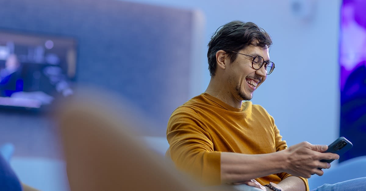 Mies katsoo hymyillen puhelinta. Mobiilivarmenne.