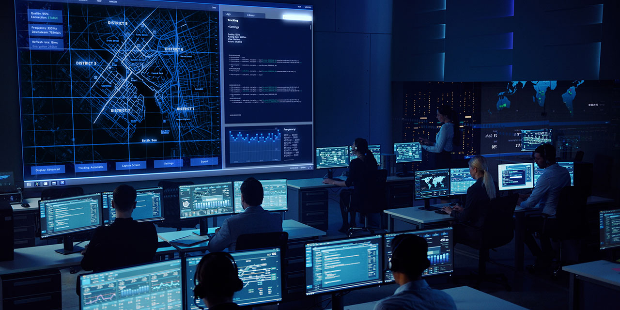 Sinisävyinen kuva, jossa ihmisiä istumassa tietokoneinen äärellä