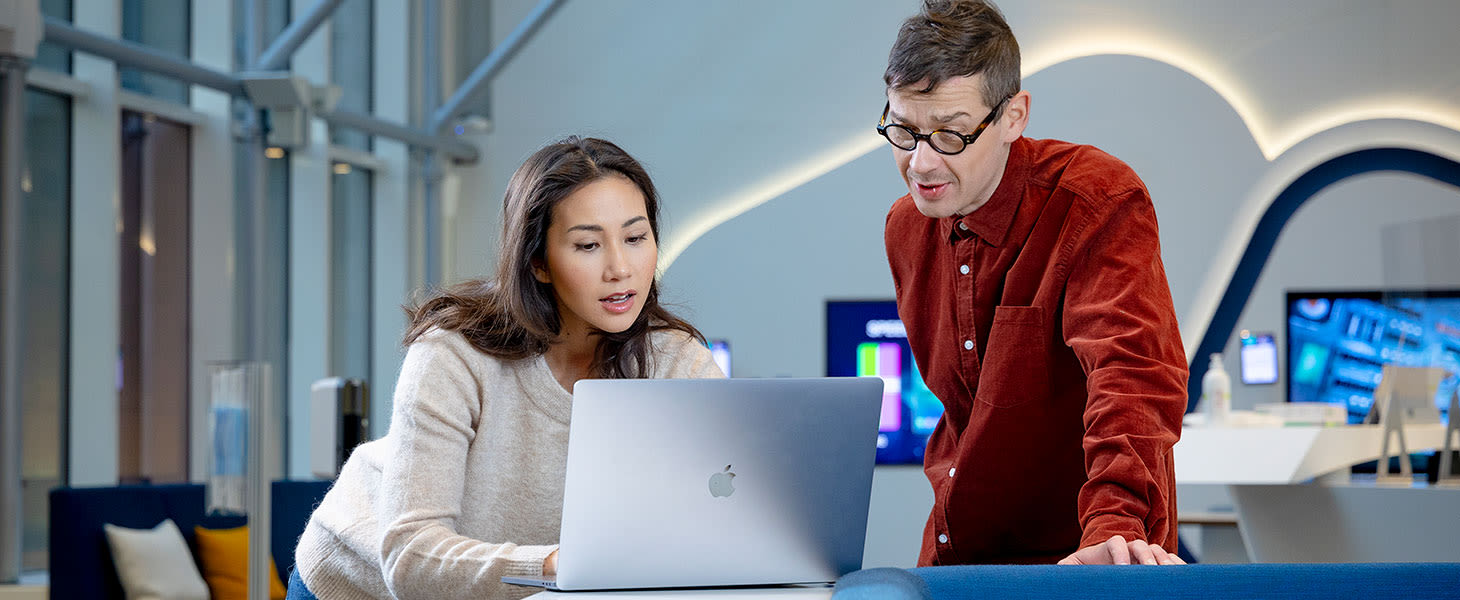 Nainen ja mies ovat avarassa aulatilassa ja katsivat kannettavan tietokoneen näyttöä.