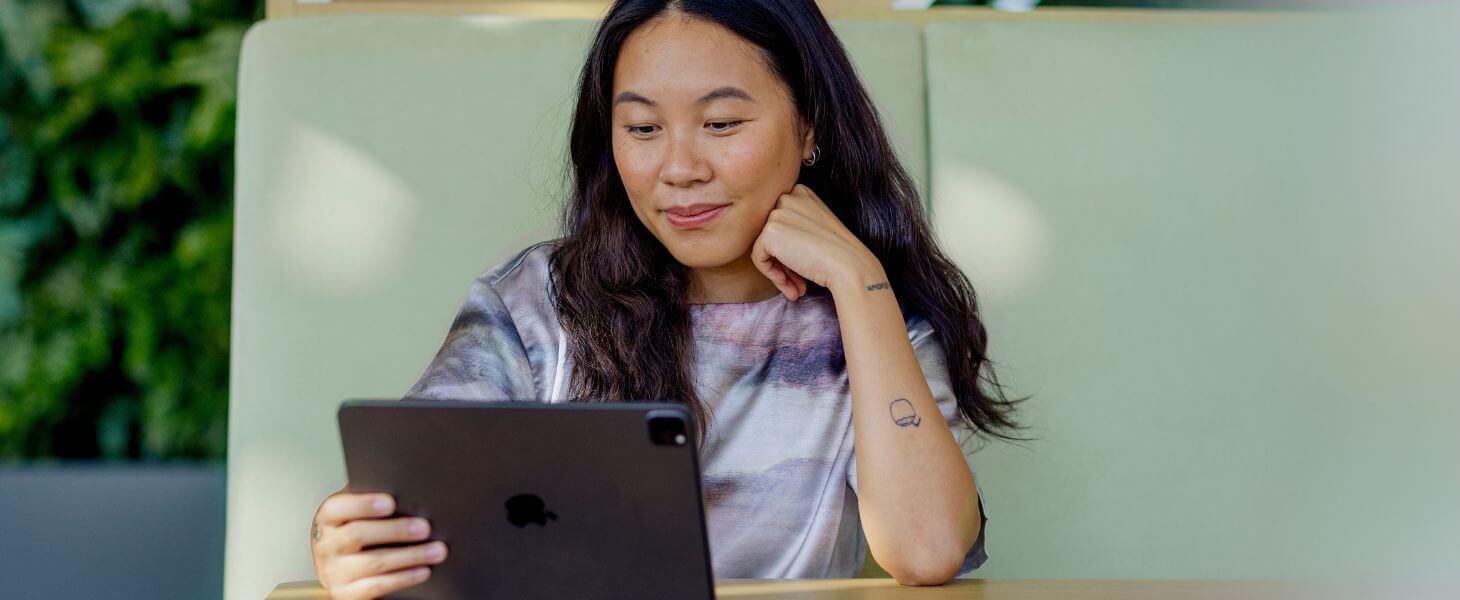 Nainen istuu vihreällä sohvalla ja katsoo tabletin ruutua, jolla on itseasioimassa asiakaspalvelussa.