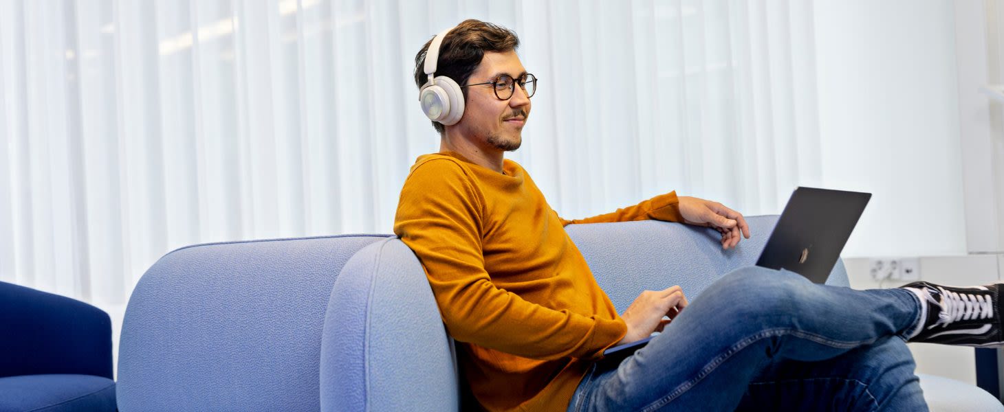 Mies istuu sohvalla kannettava tietokone sylissä ja varmistaa tietojen luokittelun tekoälyn tietoturvallista käyttöä varten, keskittyen Copilot ja tietoturva -asioihin.