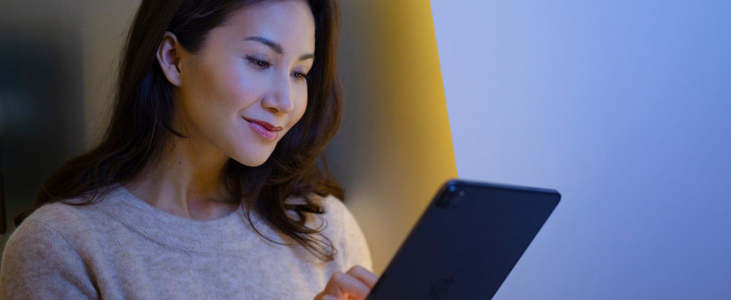 Nainen sinisellä taustalla katsoo tabletin näyttöä ja lukee tiedotetta Elisan ja Microsoftin yhteistyösopimus