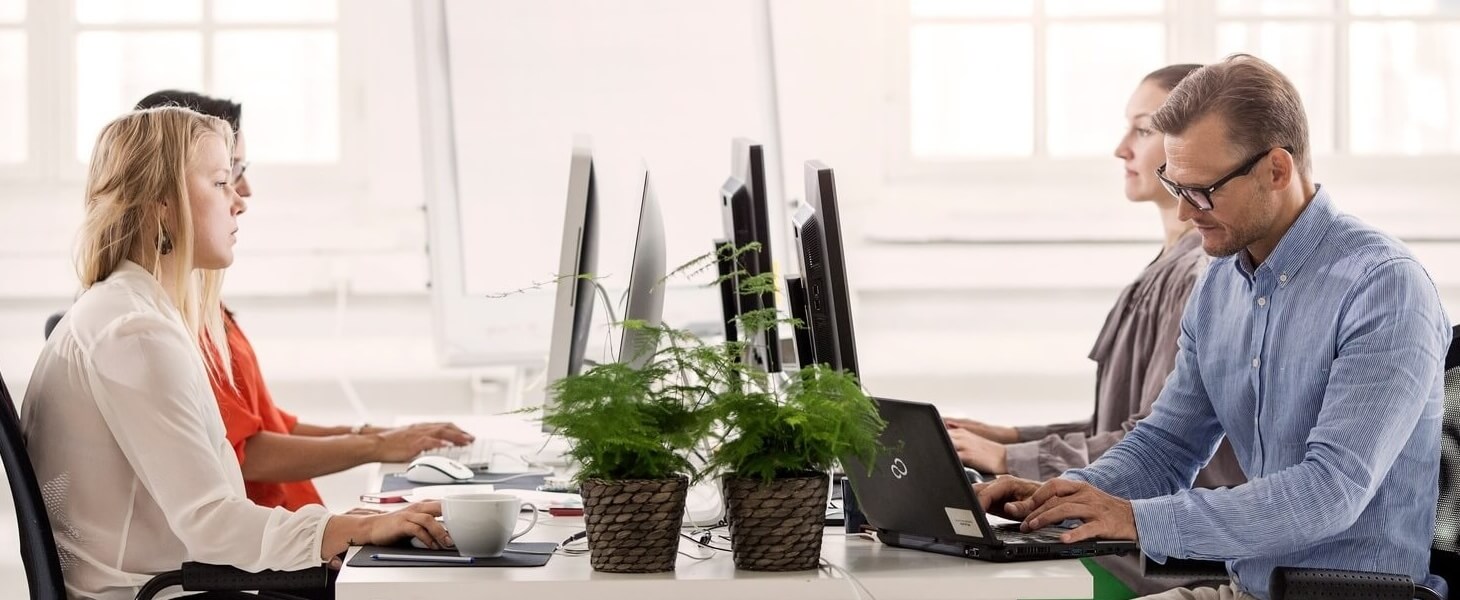 Neljä työntekijää istuvat tietokoneiden ääressä kuulokkeet korvissa kun asiakaspalvelun trendit muuttavat arkea.