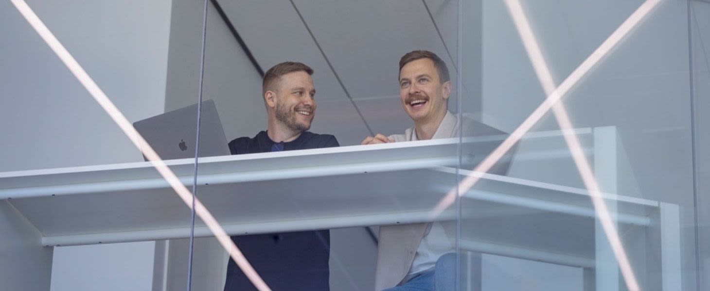 Kaksi miestä keskustelevat työpöydän ääressä ja Elisan Microsoft-osaaminen helpottaa heidän arkea.