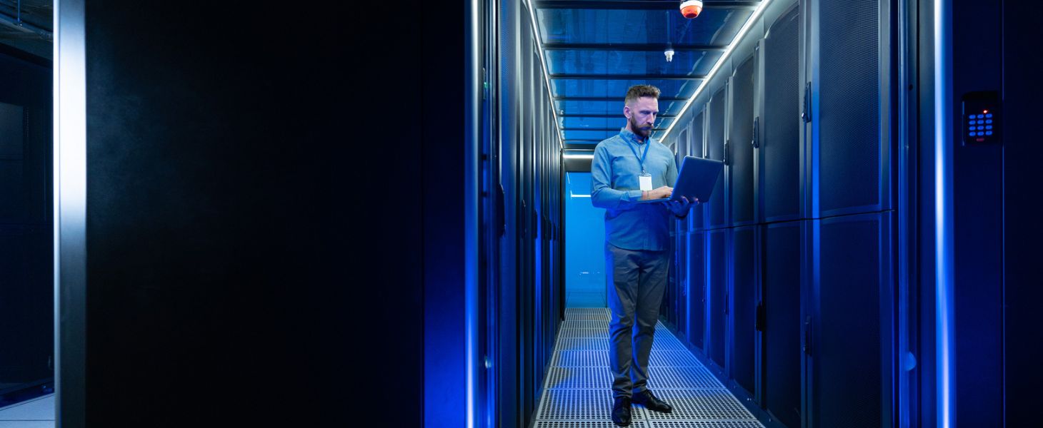 Mies seisoo kannettavan tietokoneen kanssa konesalissa, Azure-kumppanuus Elisan kanssa tukee onnistumista.