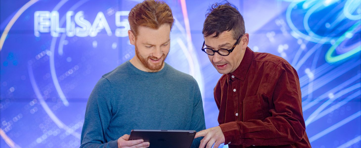 Kaksi miestä sinisen taustan edessä katsomassa tablettia, teknologiatrendit puhututtavat.